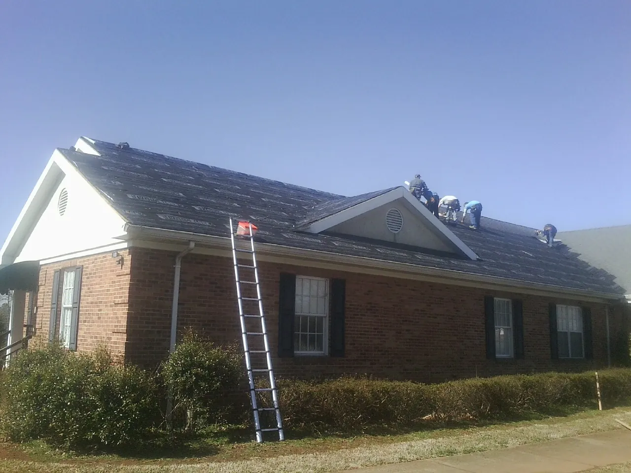 Crew tearing shingles off a brick ranch roof with a ladder set — Metal Roof Repair work by our crew in Upper Black Eddy