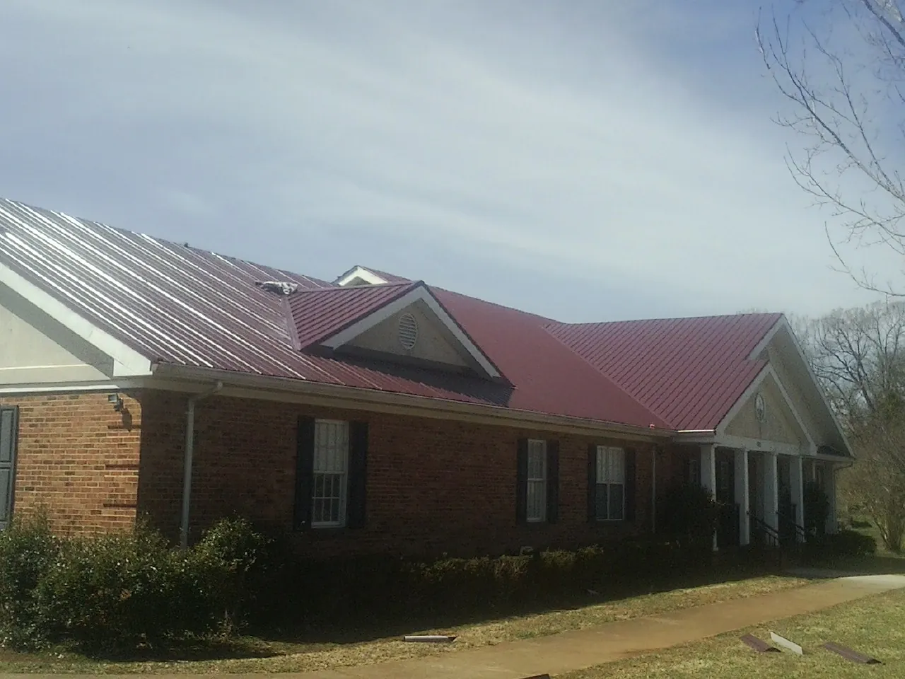 Red metal roof with gabled entries on a long brick building, from a Hail Damage Roof Repair job in Upper Black Eddy
