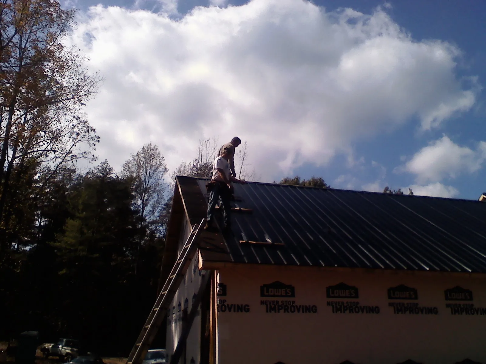 Roofer fastening dark metal panels high against a cloudy sky, from a Roof Inspection job in Upper Black Eddy