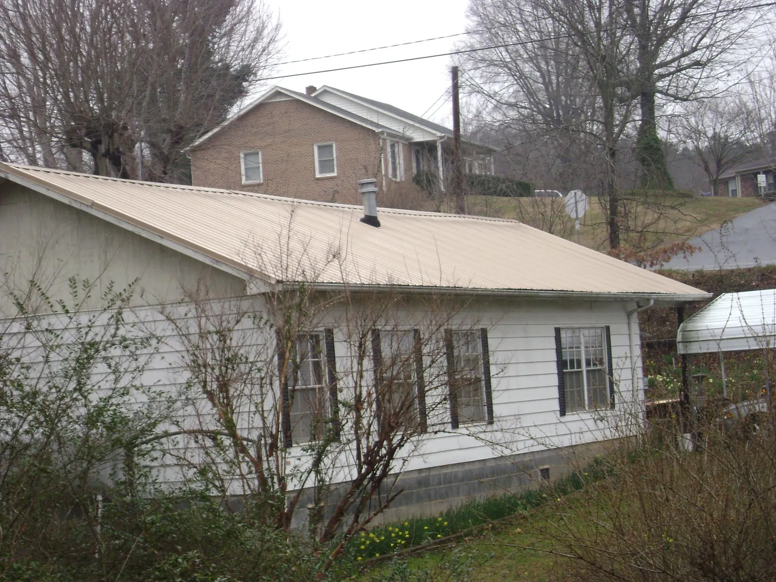 Tan metal roof on a white sided house set into a hillside — Commercial Roofing by Roofing Brothers in Upper Black Eddy
